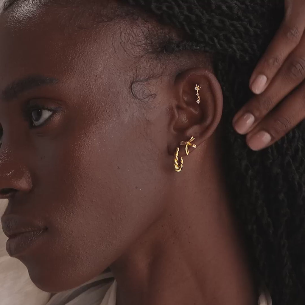 Model showcasing a dainty gold bow stud earring, stacked with a gold twisted hoop earring and a pavé star drop stud earring.