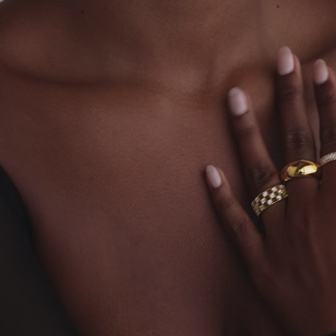 Model showcasing a gold checkered diamond ring with an open grid design and sparkling round-cut stones, stacked with matching gold rings.
