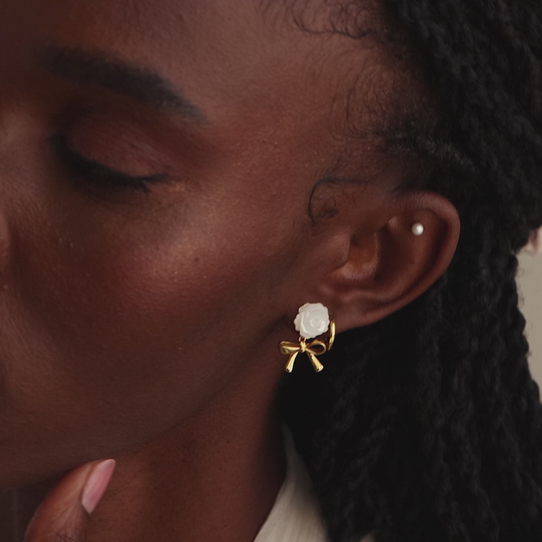 Model showcasing white rose and gold bow drop stud earrings with a pearl stud and huggie hoop to complete the look.