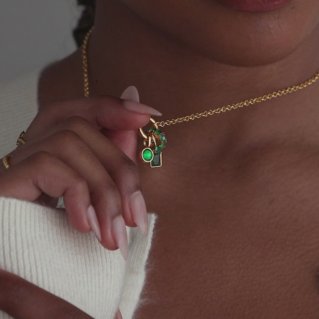 Model wears a gold rolo chain with an assortment of emerald birthstone charms