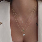 Model wearing a dainty gold North Star Birthstone Necklace in Opal layered with a starburst charm necklace and delicate CZ diamond necklace.