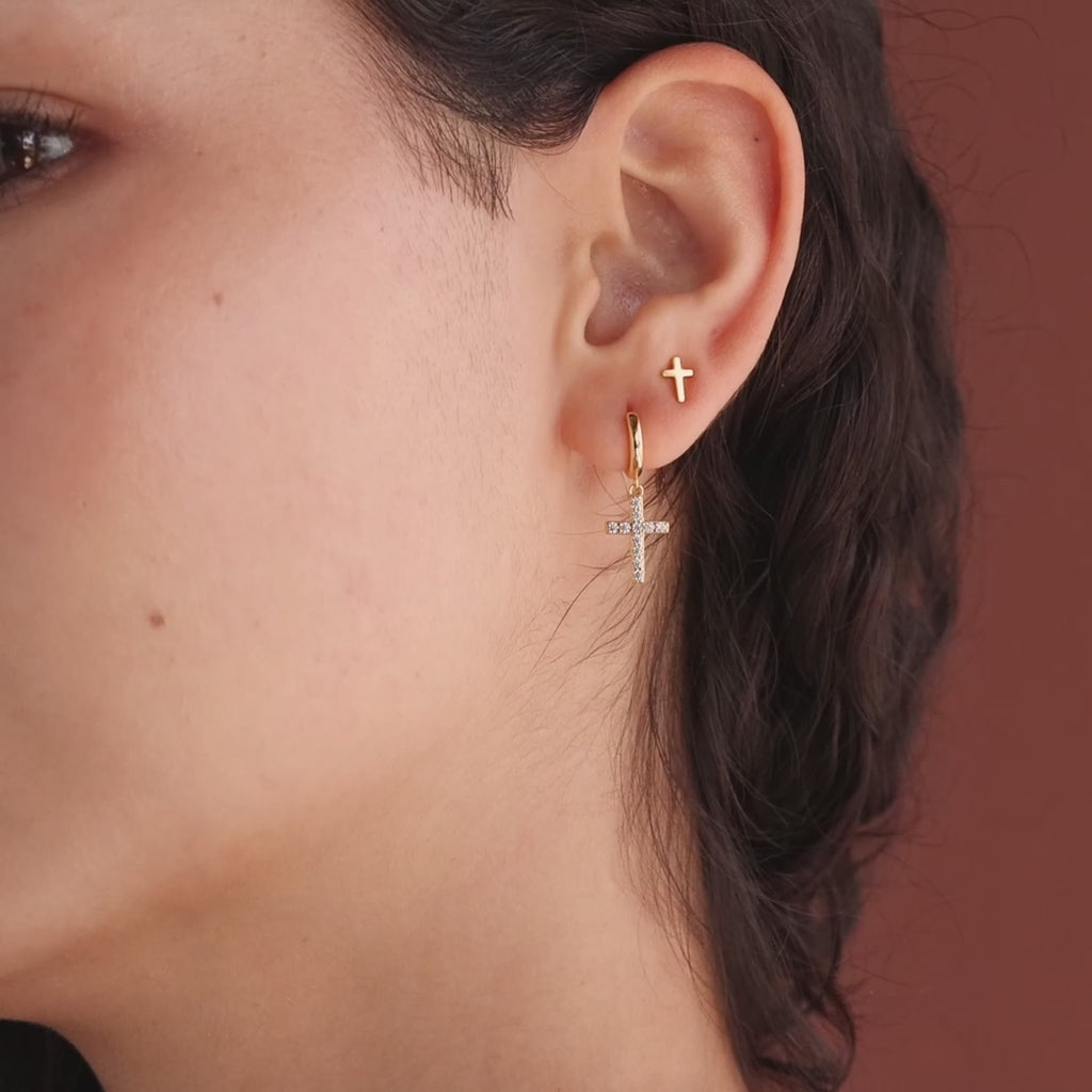 Model showcasing dainty gold cross stud earrings, styled with gold pave cross huggie hoops.