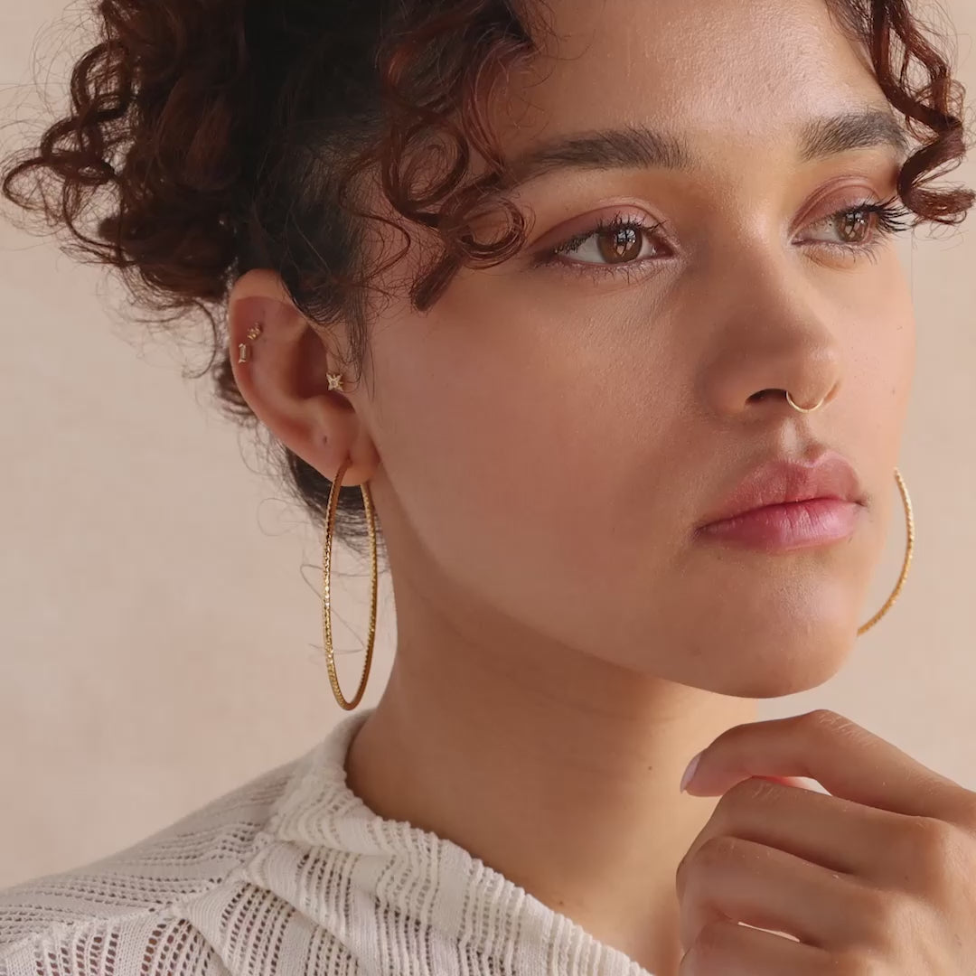 Textured gold hoop earrings make a bold yet elegant statement, catching the light beautifully with their faceted design.