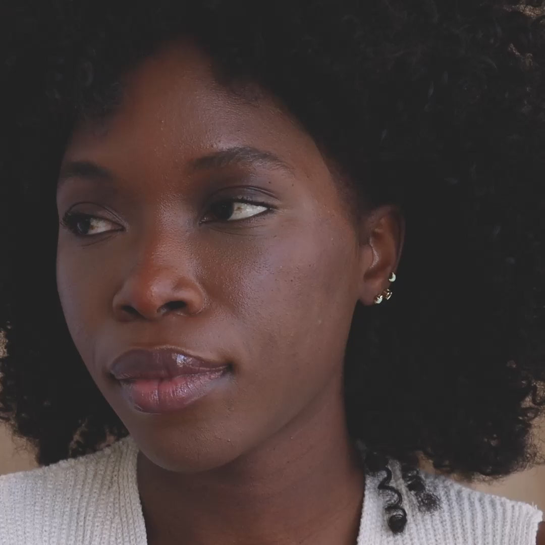Model wearing mismatched set of 3 dainty gold Opal and CZ Diamond Celestial Earrings with moon, heart, and star studs.
