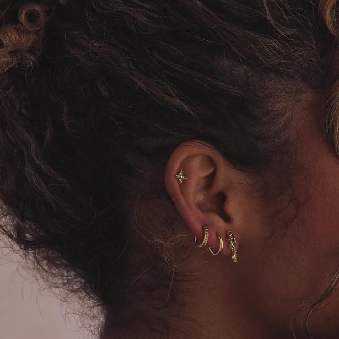 Model showcasing gold marquise-cut drop stud earrings with green peridot gemstones, stacked with multiple matching gold earrings.