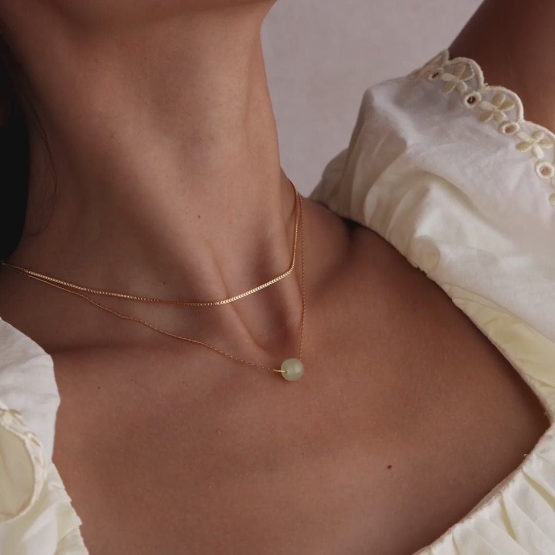 Model showcasing a delicate gold chain necklace featuring a single round green jade bead, layered with a dainty box chain necklace.