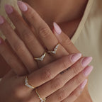 Model showcasing multiple gold rings, featuring a V-shaped pavé diamond ring on the middle finger.