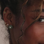 Model showcasing a green jade stud earring with a centered CZ diamond, styled with multiple gold hoop and stud earrings.