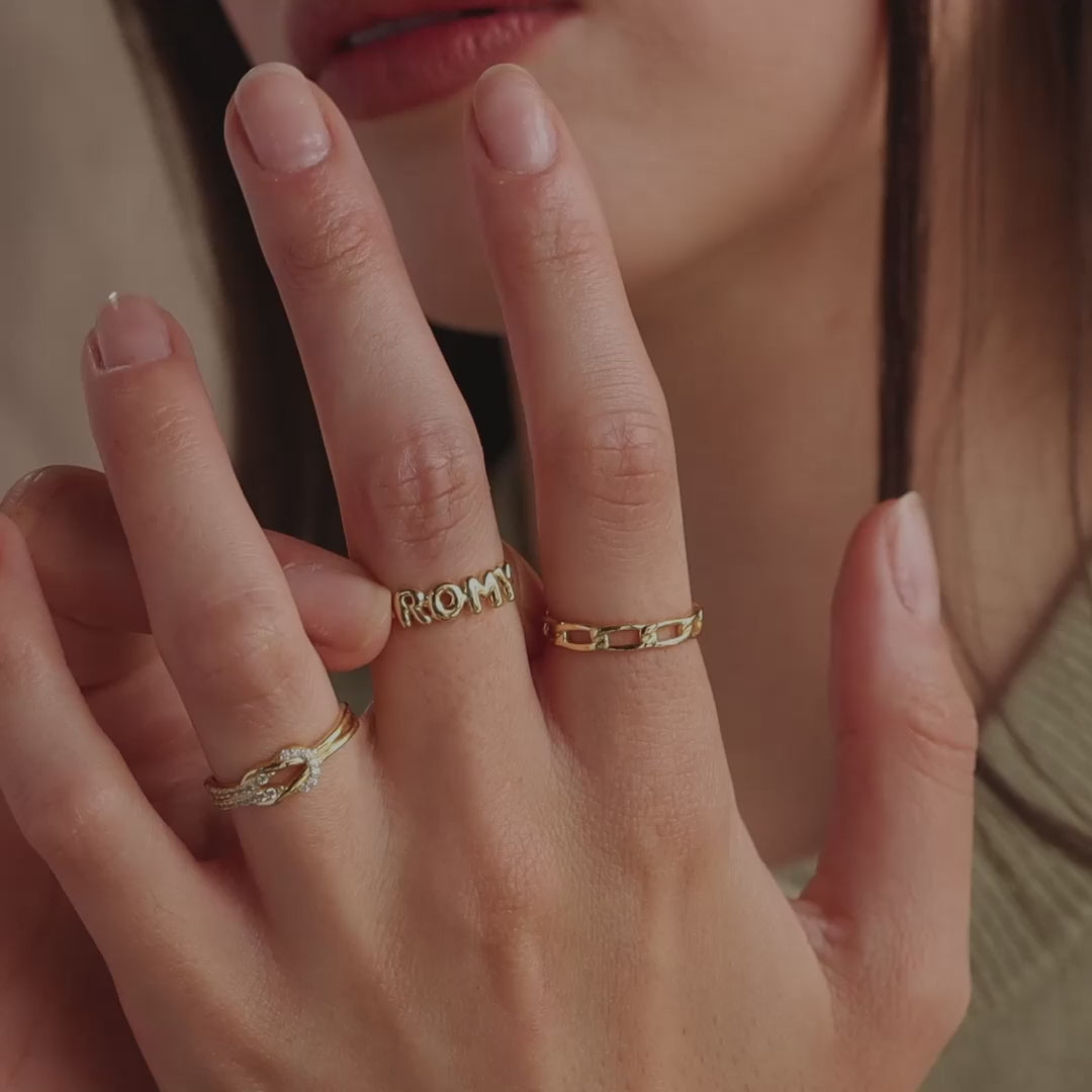 Model wearing a dainty gold bubble letter ring with the name "ROMY", styled with a gold pave knot ring and a gold link chain ring.
