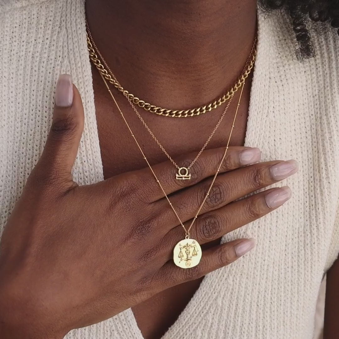 Model wearing gold CZ diamond Libra Zodiac Charm Necklace layered between a chunky bold curb chain necklace and a matching Libra Zodiac Coin Necklace.