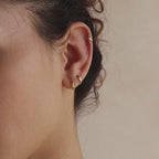 Close-up of model's ear with three dainty gold huggie hoop earrings in multiple sizes.