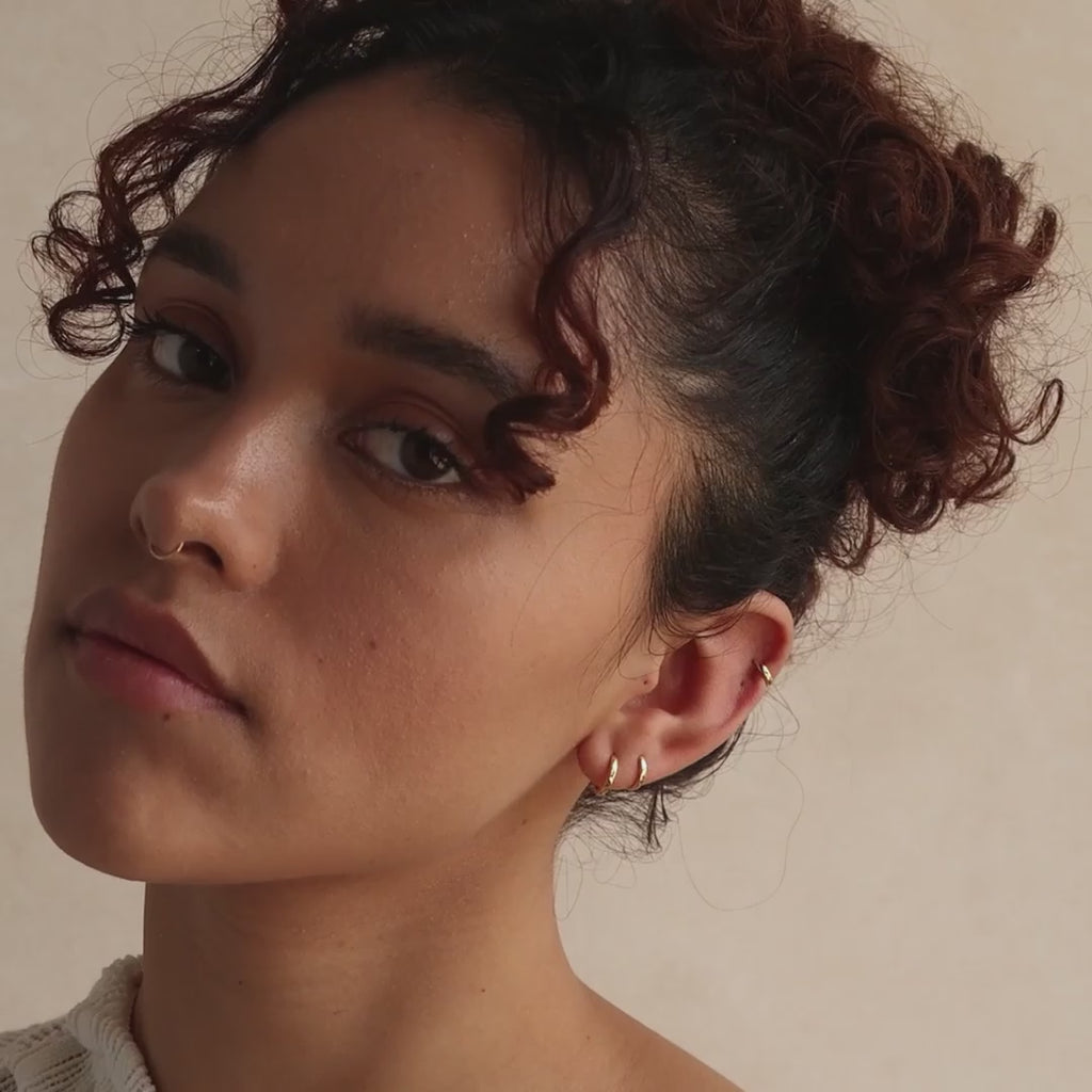 Close-up of model wearing three gold huggie hoop earrings in her lobe and one in her cartilage, showcasing a stacked ear look.
