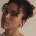 Close-up of model wearing three gold huggie hoop earrings in her lobe and one in her cartilage, showcasing a stacked ear look.