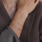 Model wearing a gold dainty bubble initial K bracelet stacked with a flower station bracelet, and layered with delicate gold necklace and matching rings.
