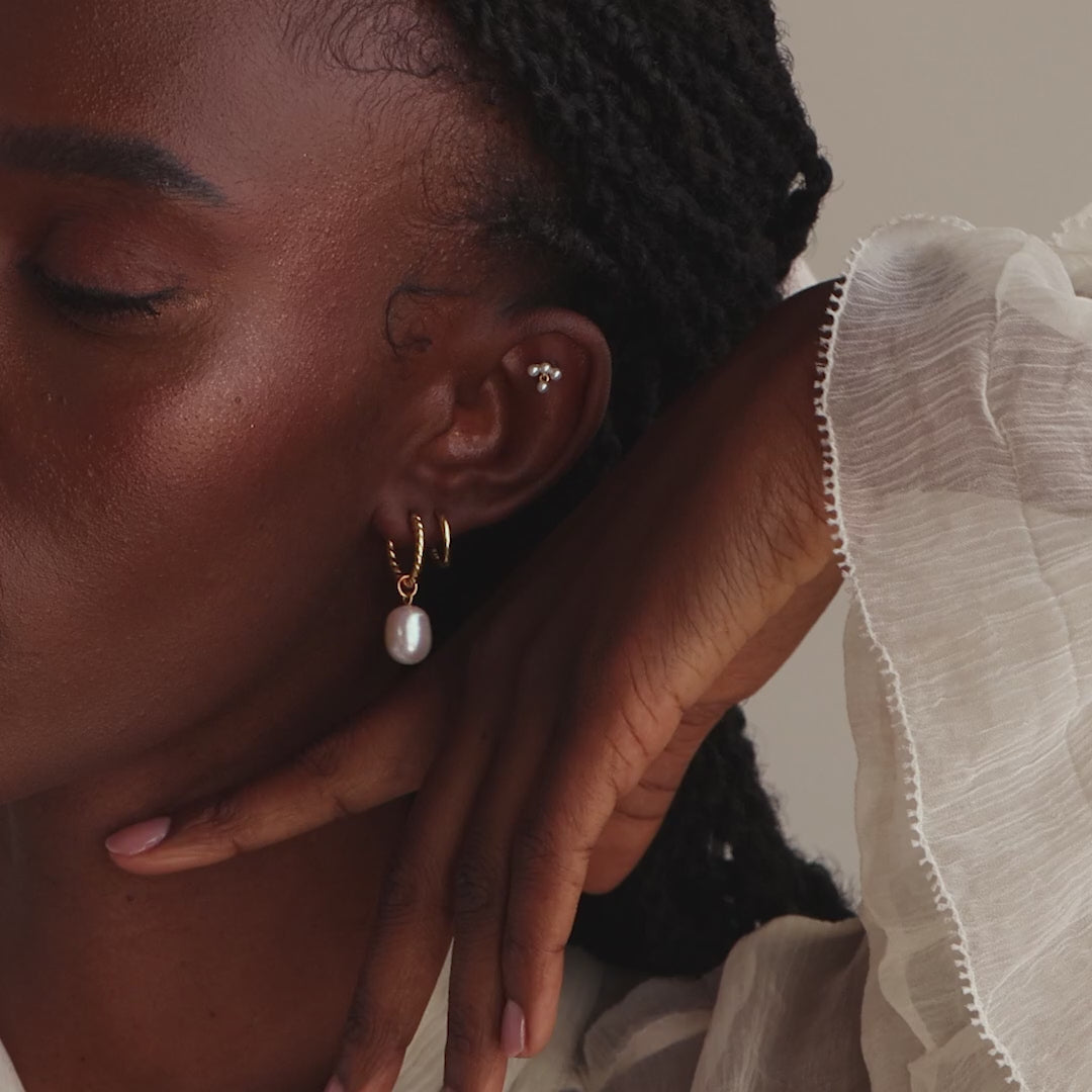 Model showcasing the gold twisted pearl hoop earrings, stacked with a gold hoop earring and pearl cluster drop stud earring.