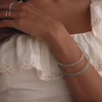 Model showcasing a set of two thin jade bangles in soft translucent green tones, styled with multiple gold rings.