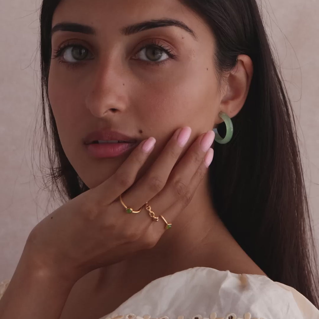 Model showcasing Jade Hoop Earrings, featuring a chunky hoop design with a soft green natural jade gemstone, styled with multiple gold rings.