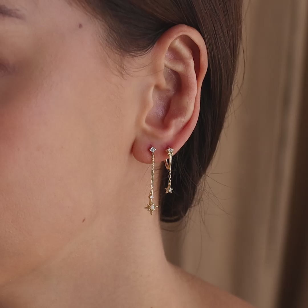 Model wearing gold starburst chain stud earrings, accompanied by another star earring on a second piercing.