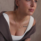 Model wearing a dainty gold bubble puff letter name plate necklace layered with a beaded necklace and pavé duo circle necklace.