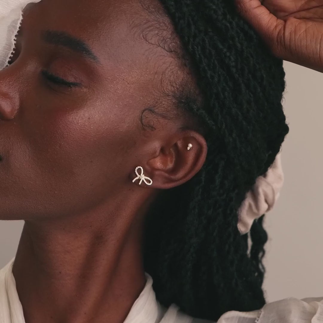 Model wearing gold pavé bow stud earrings paired with a dainty pearl and diamond stud earring.