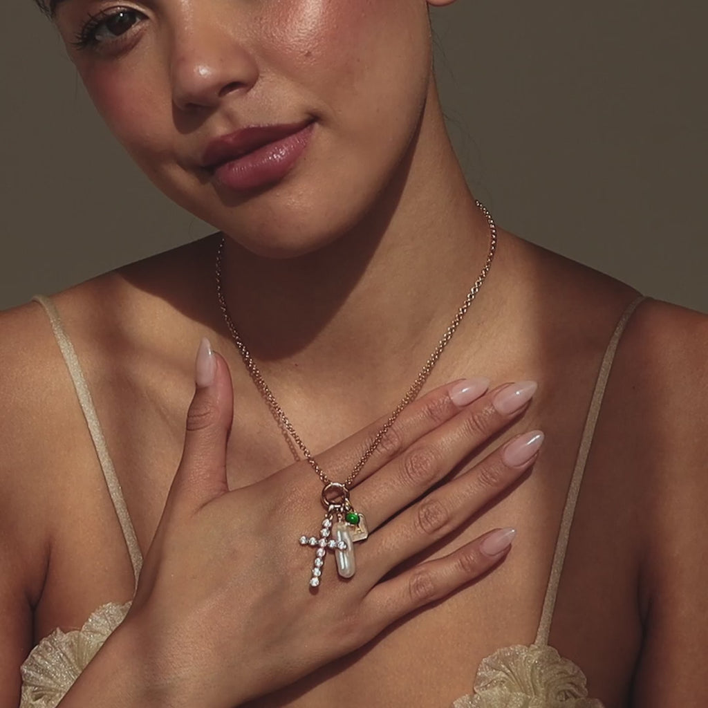 Video of model wearing gold Rolo Necklace with gold Pave Cross Charm and an assortment of other pendants, such as a gold long pearl charm, emerald birthstone charm and initial charm