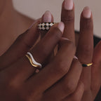 Model showcasing a gold dome ring with black and white checkered enamel pattern, stacking with multiple gold rings.
