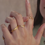 Detailed shot of stacked gold rings on hand, featuring a custom double initial ring with bubble letters K and J and a mix of textured and chevron bands.