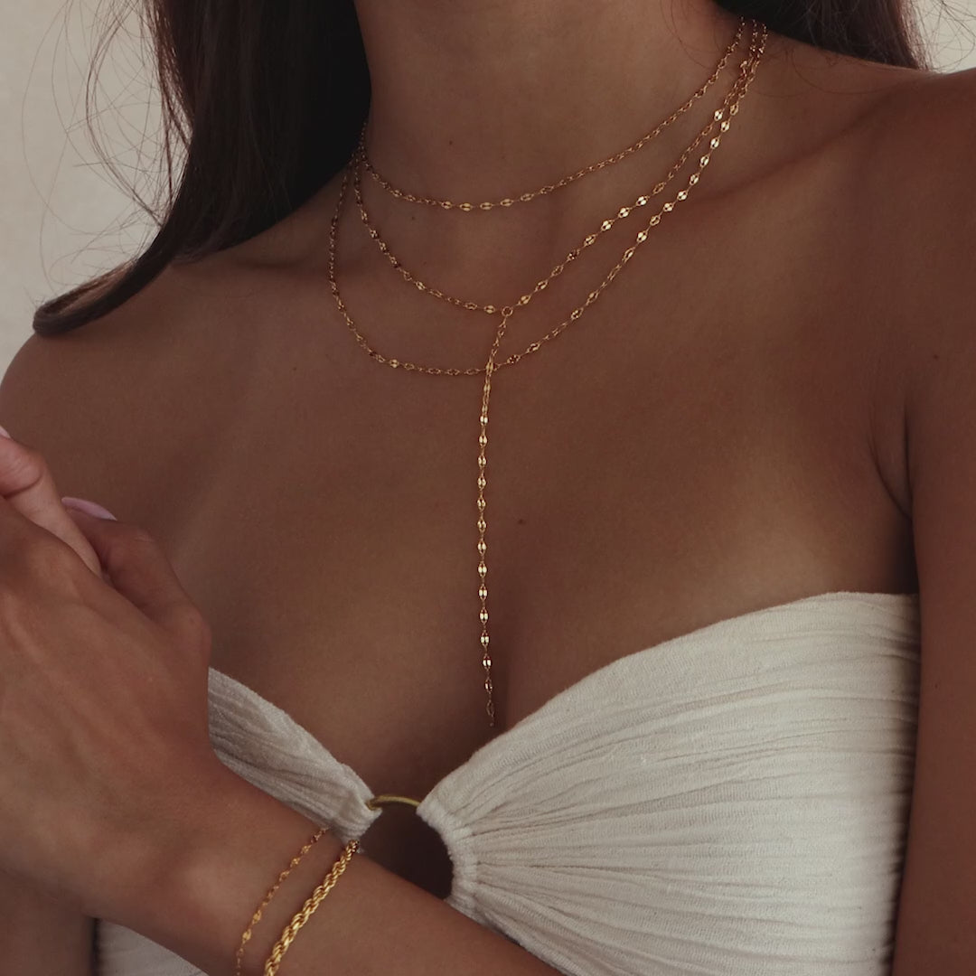 Model showcasing a gold dainty Sparkling Layered Lariat Necklace, featuring 3 layers of mirror chain necklaces in varying lengths, styled with 2 gold bracelets.