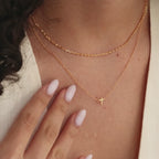 Model showcasing a dainty gold cross charm necklace, layered with a gold mariner chain necklace.