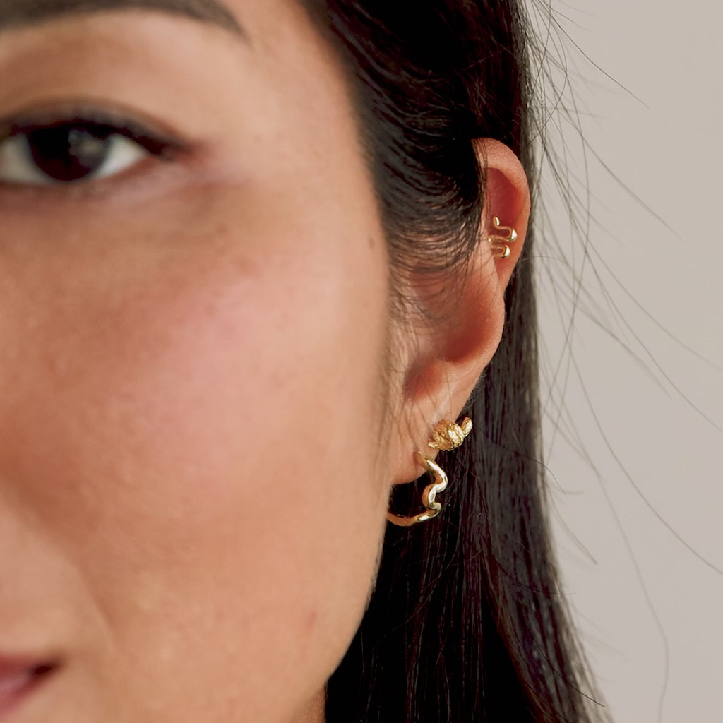 Model showing an ear styling with multiple piercings. The gold Twisted Snake Earring is worn on the lower lobe, paired with other minimal snake earrings along the cartilage and upper ear