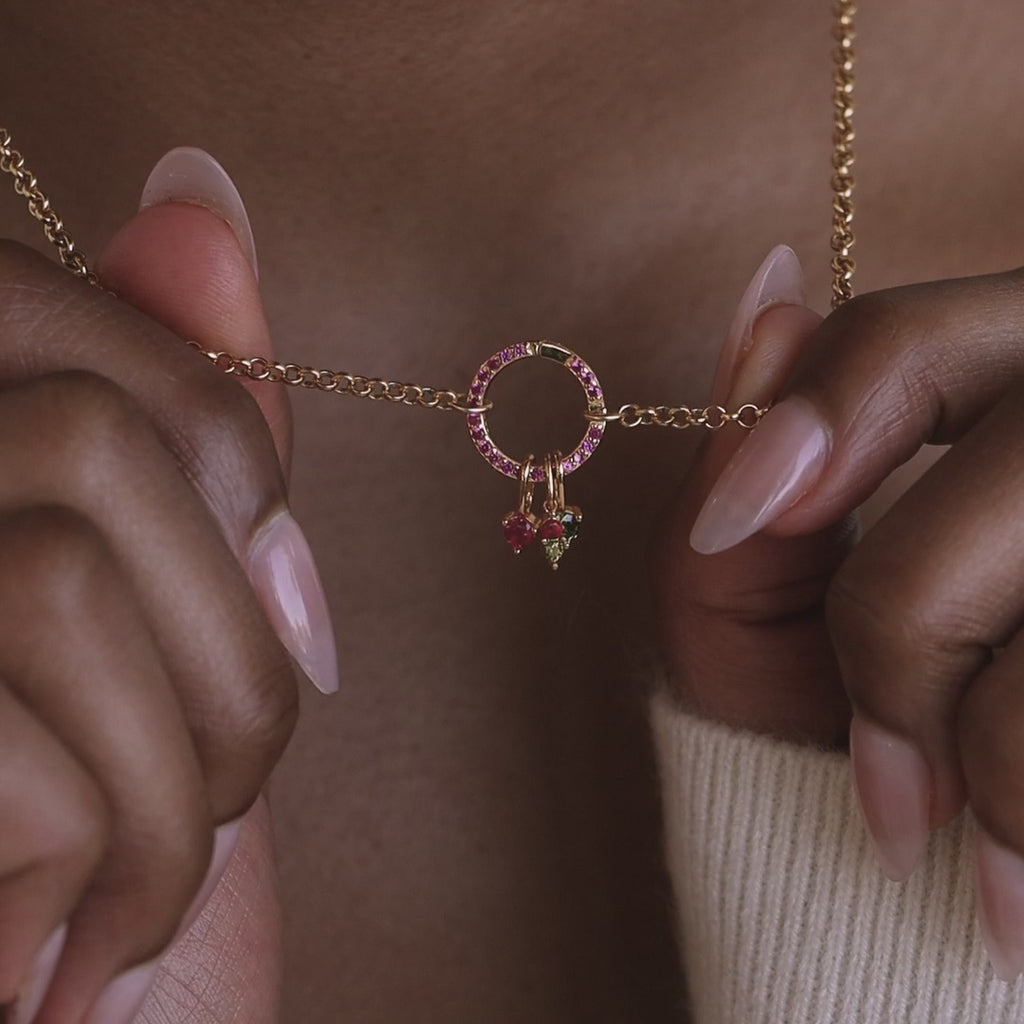 Model holds up a cable chain with a pave birthstone rolo clasp. The clasp has dangling birthstone charms on it