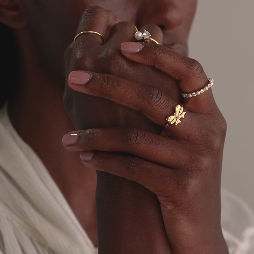 A model wears the Bow Pearl Ring paired with other gold rings, showcasing a layered, chic jewelry styling.