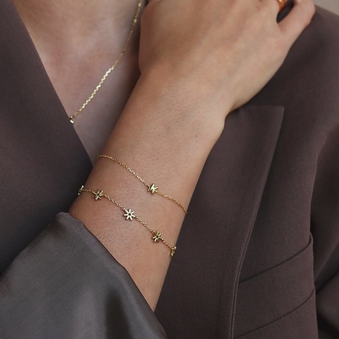 Model wearing a gold dainty bubble initial K bracelet stacked with a flower station bracelet, and layered with delicate gold necklace and matching rings.
