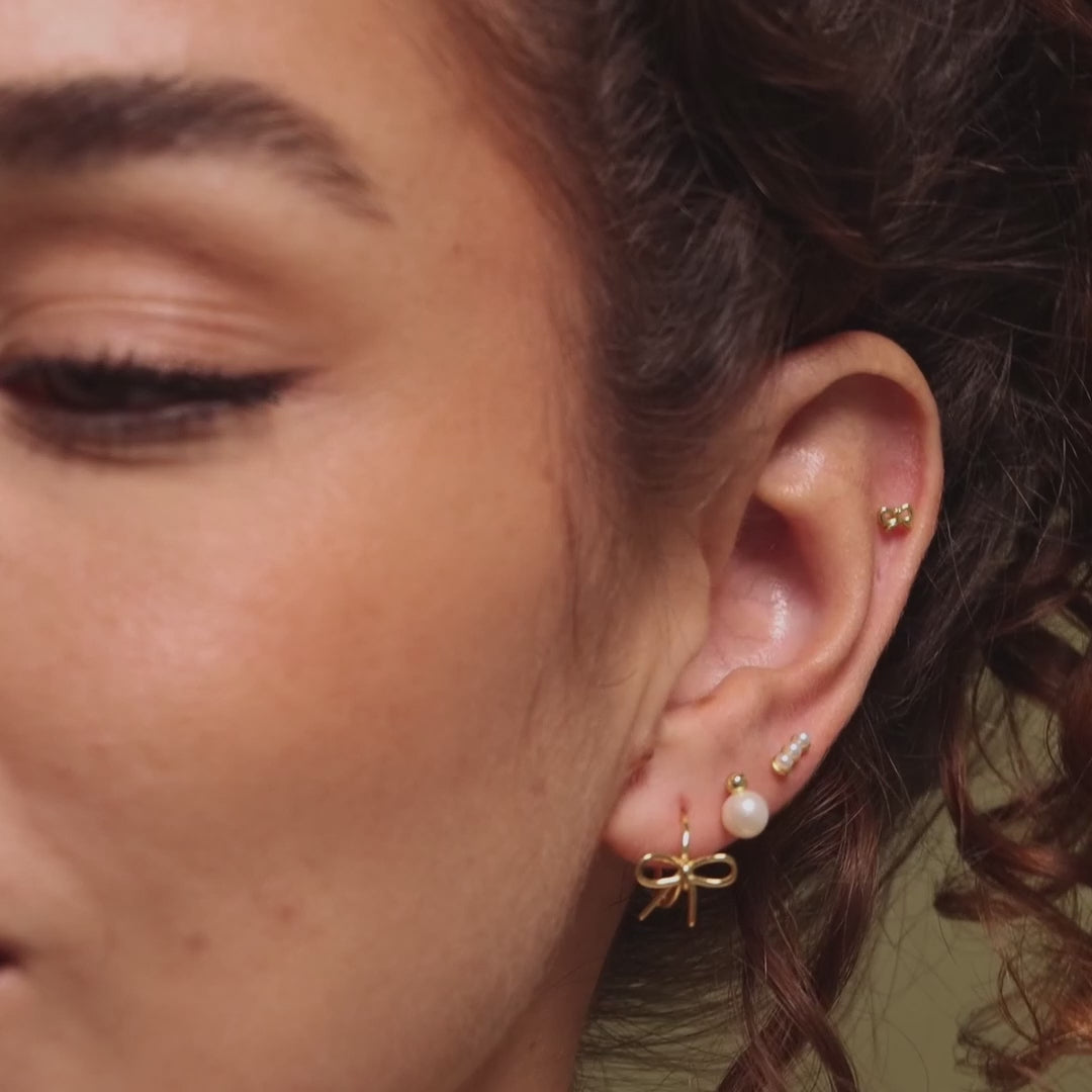 Video of a model wearing our Tiny Bow Flatback Studs in 18K Gold, styled with our Pearl Studs and Bow Huggies