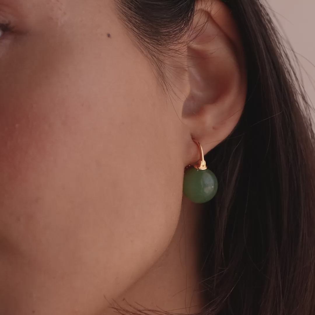 Model showcasing gold Jade Dome Drop Earrings featuring rounded green gemstones on dainty hoops, styled with multiple gold rings.