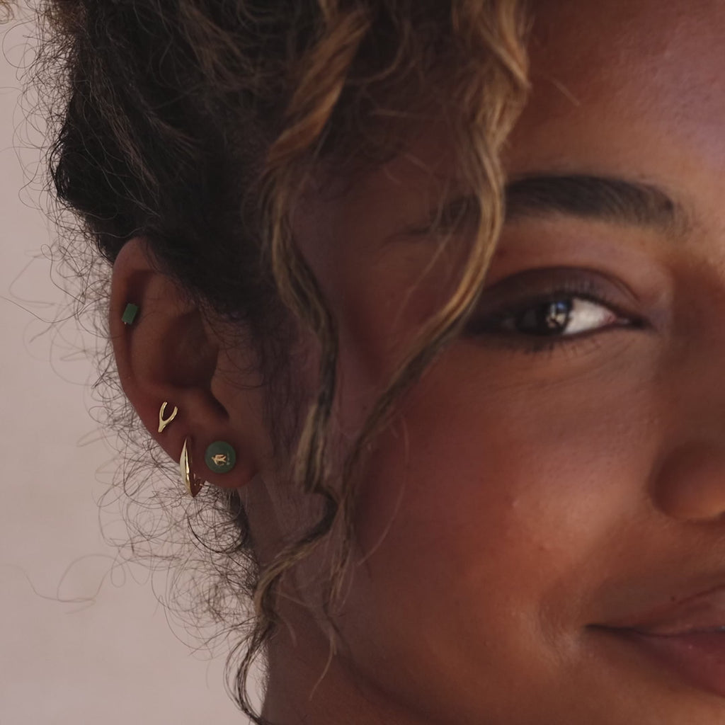 Model showcasing gold Jade Bird Stud Earrings with a dainty golden dove birds on a round green jade discs, stacked with multiple gold and jade stud earrings.