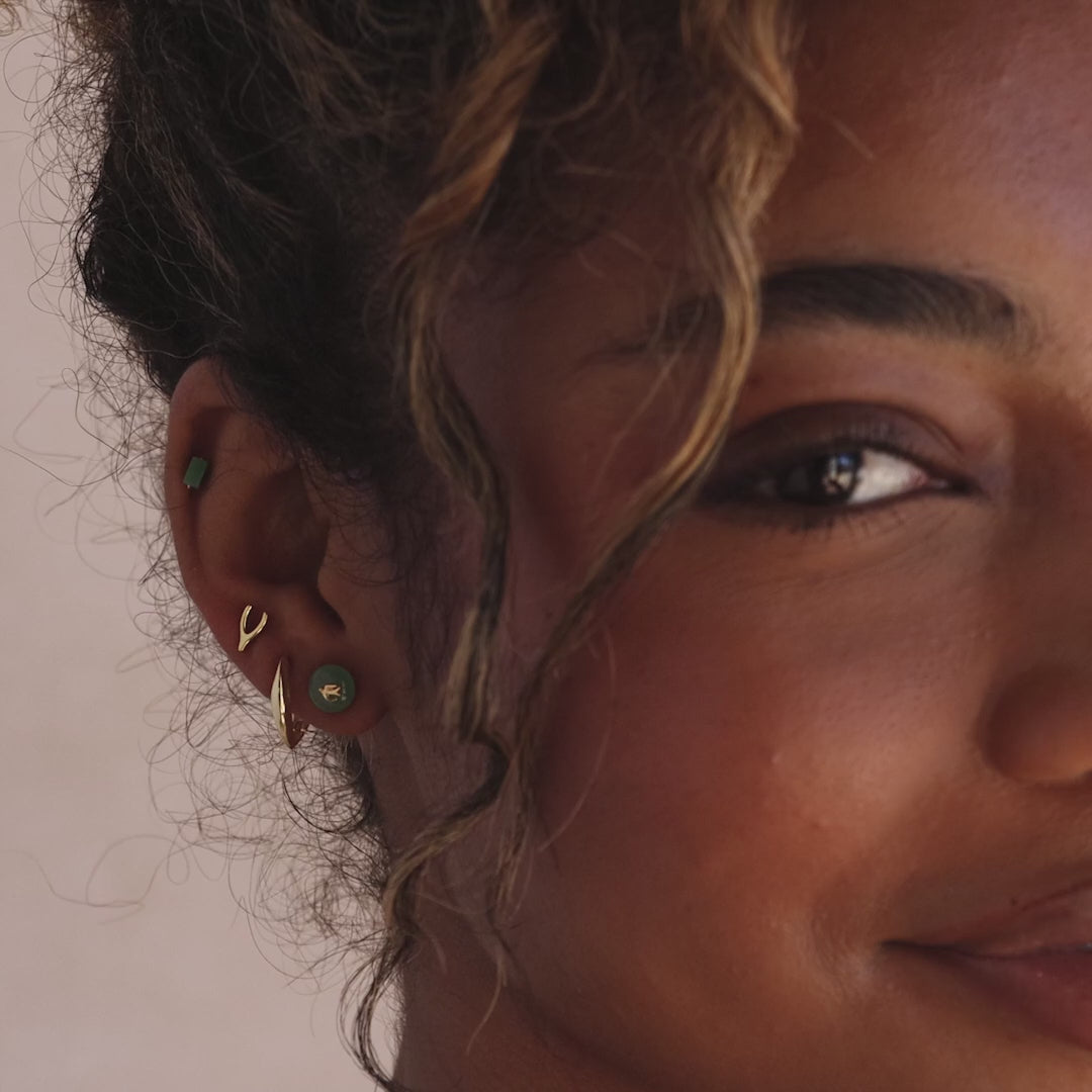 Model showcasing gold Jade Bird Stud Earrings with a dainty golden dove birds on a round green jade discs, stacked with multiple gold and jade stud earrings.