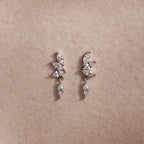 Dainty silver CZ diamond drop earrings with four marquise-cut stones, displayed on a neutral surface.