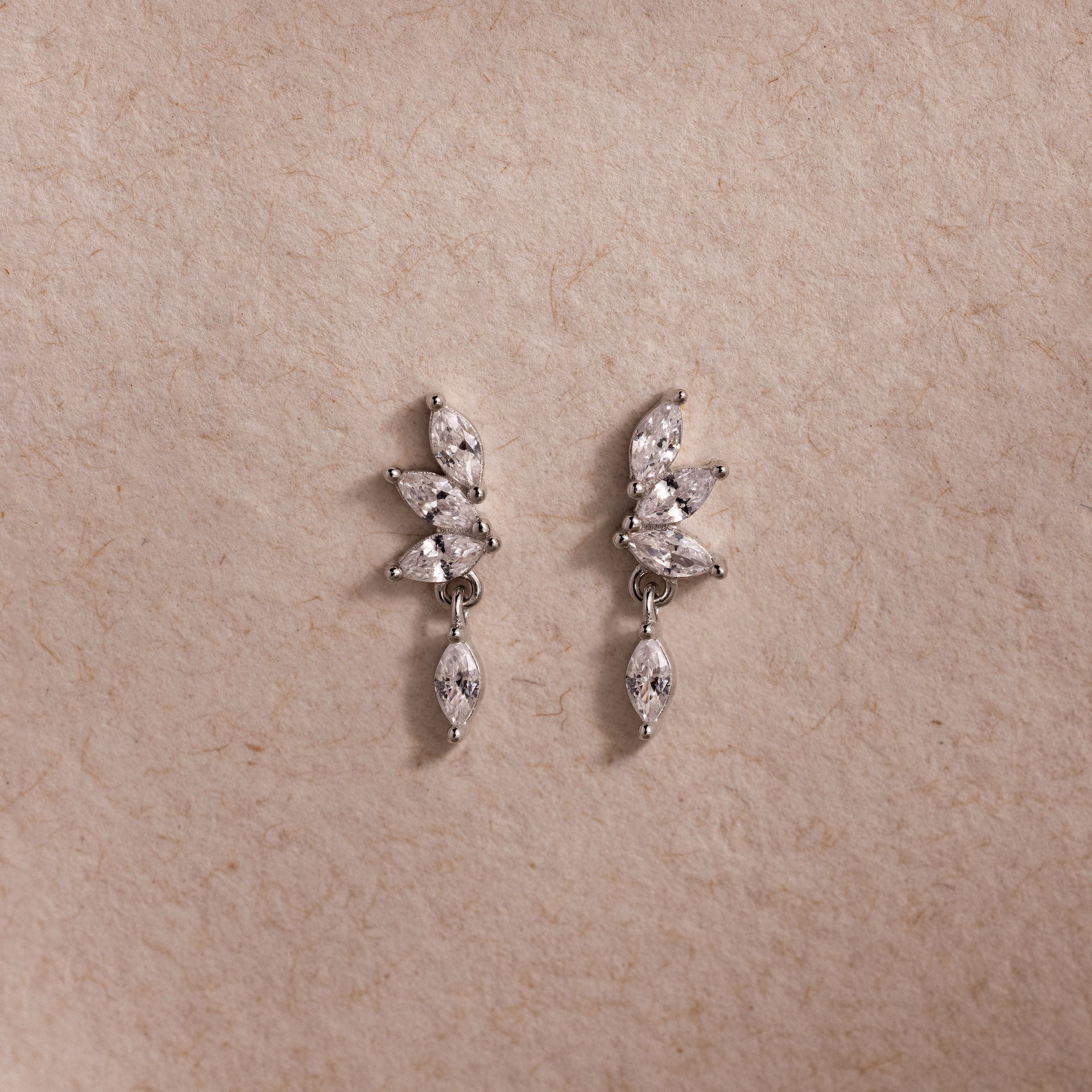 Dainty silver CZ diamond drop earrings with four marquise-cut stones, displayed on a neutral surface.