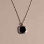 Silver chain necklace featuring a square black onyx pendant in a textured gold bezel, displayed against a neutral background with soft lighting.