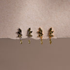 Two pairs of marquise-cut drop earrings in gold and silver, each with green peridot gemstones arranged in a cascading leaf-inspired design, displayed on a soft cream fabric.