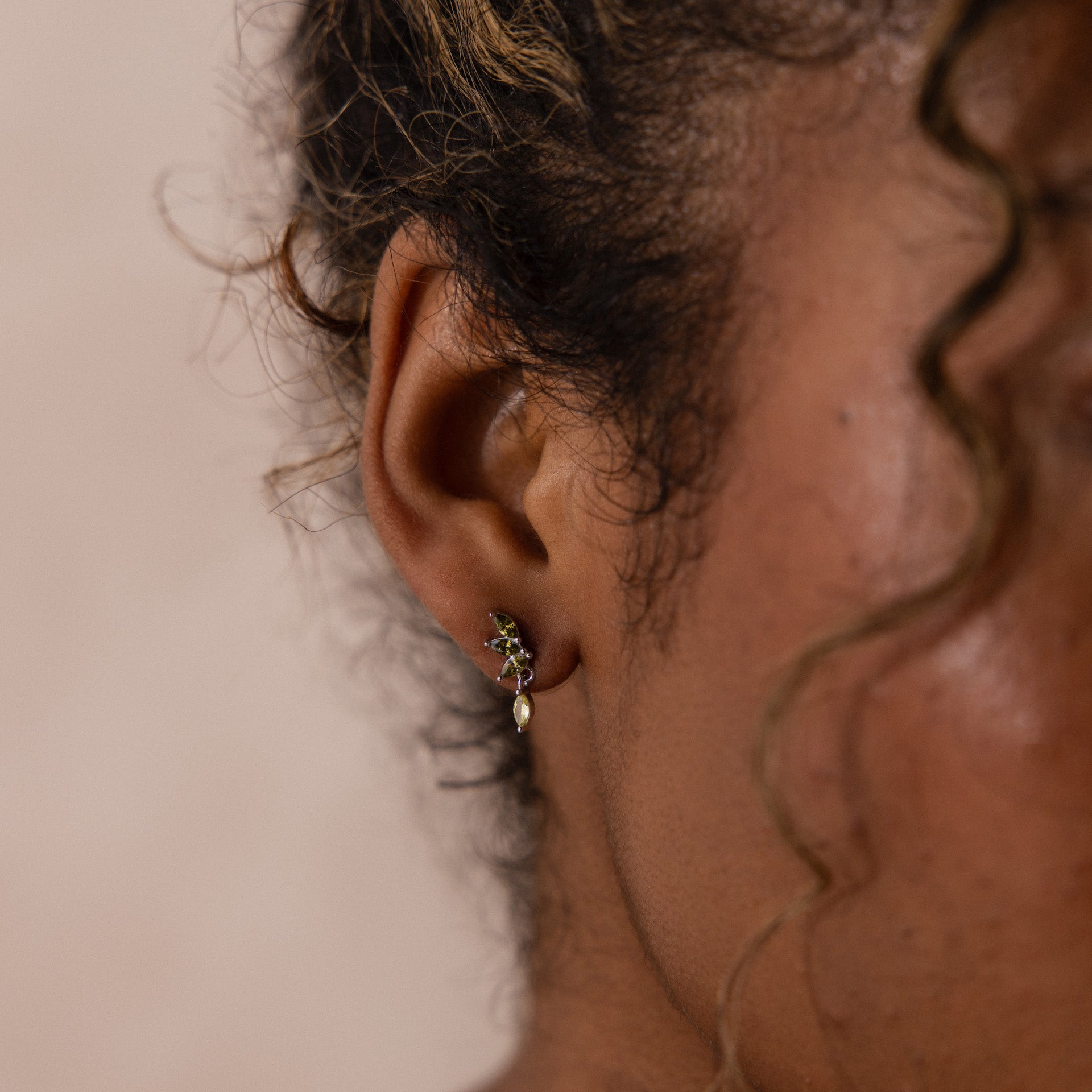 Model wearing silver marquise-cut drop earrings with green peridot gemstones arranged in a cascading leaf-inspired design.