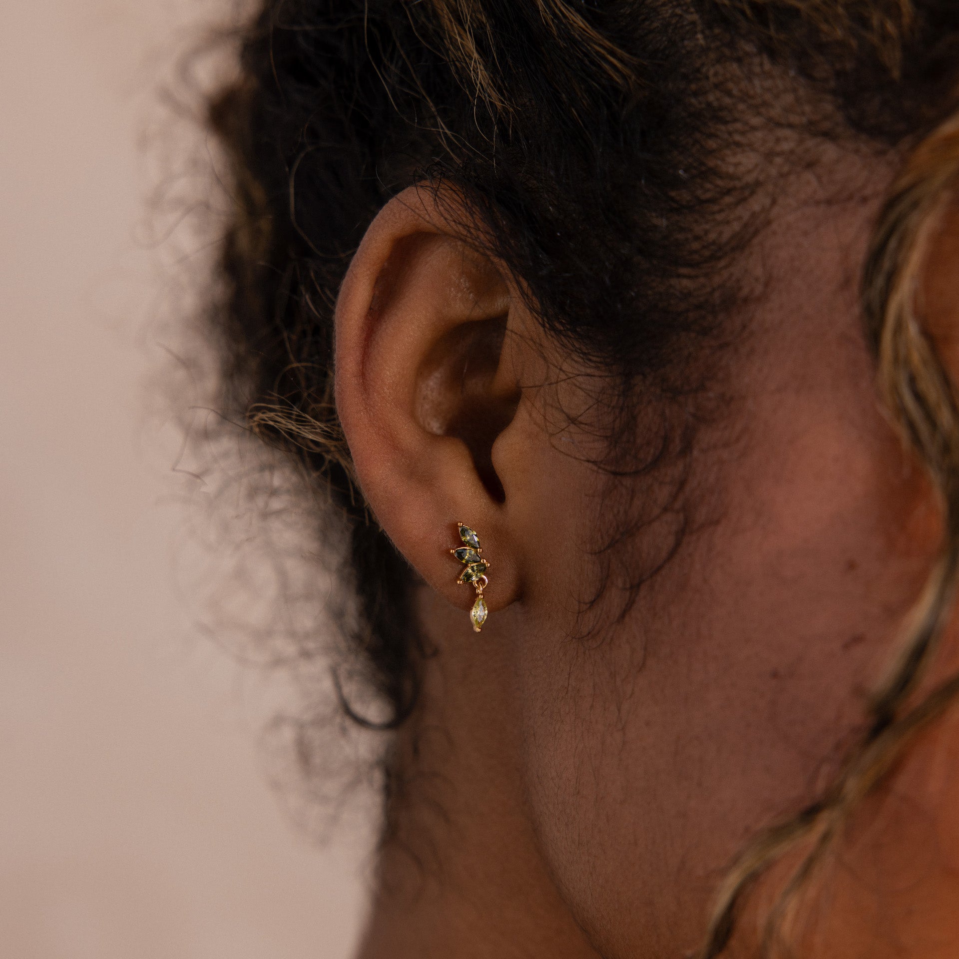 Model wearing gold marquise-cut drop earrings with green peridot gemstones arranged in a cascading leaf-inspired design.