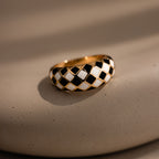 Gold dome ring with black and white checkered enamel pattern, displayed on a neutral stone surface.