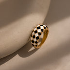 Gold dome ring with black and white checkered enamel pattern, displayed up-right against a neutral surface.