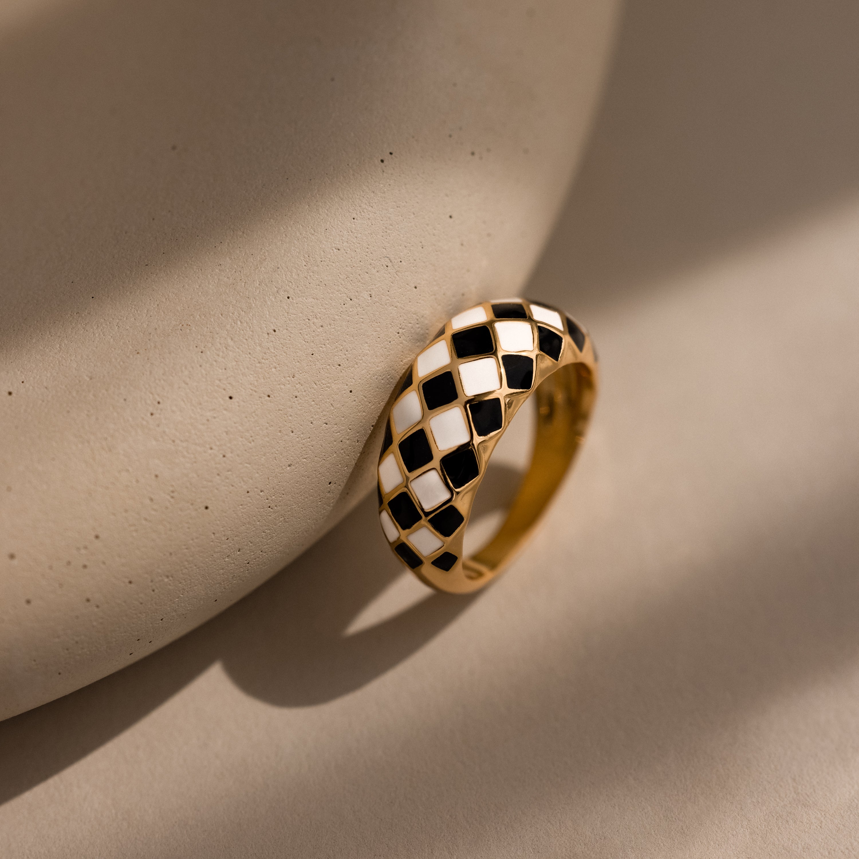 Gold dome ring with black and white checkered enamel pattern, displayed up-right against a neutral surface.