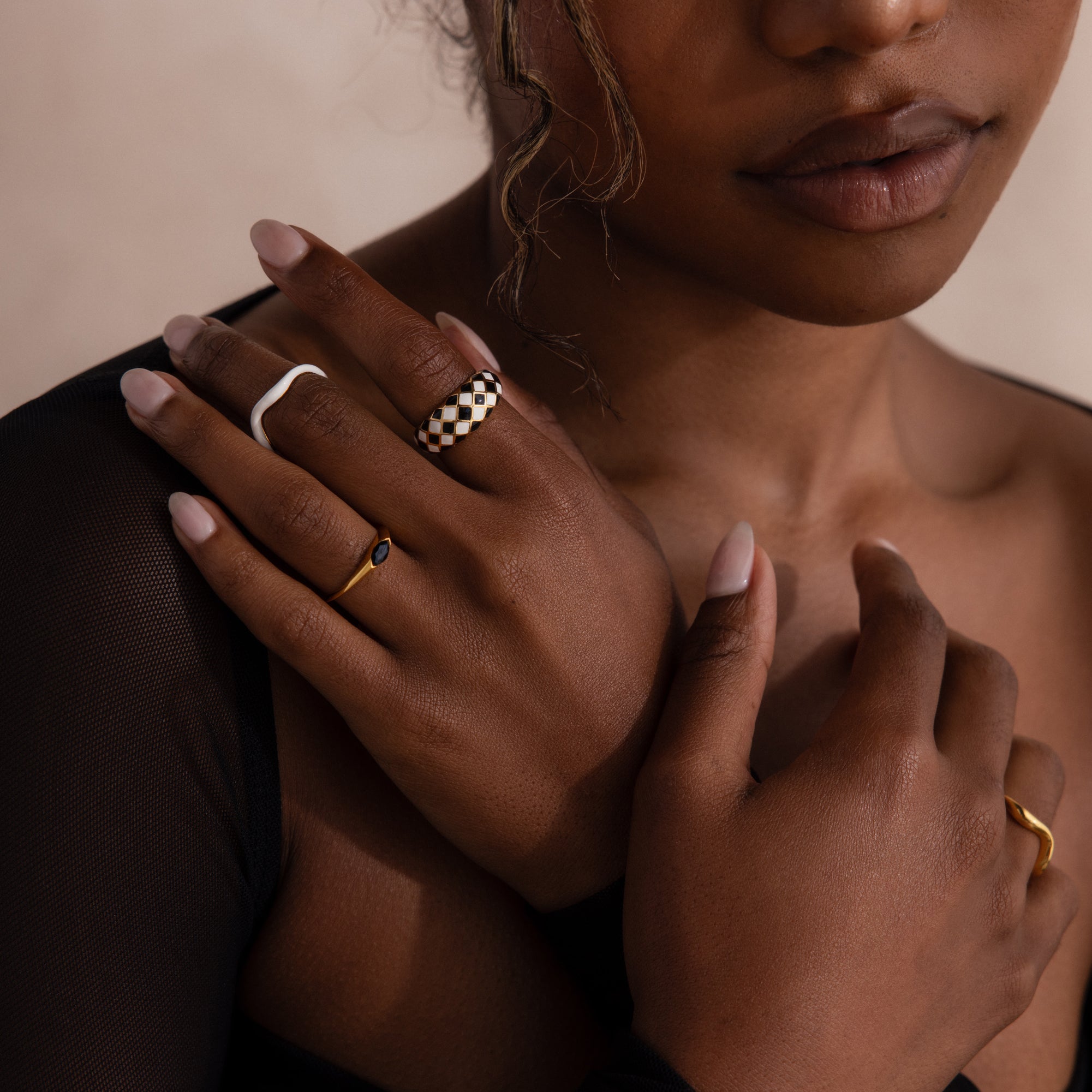 Model wearing a gold dome ring with black and white checkered enamel pattern, stacking with multiple gold rings.