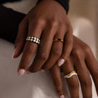 Model wearing a gold dome ring with black and white checkered enamel pattern, stacking with multiple gold rings.