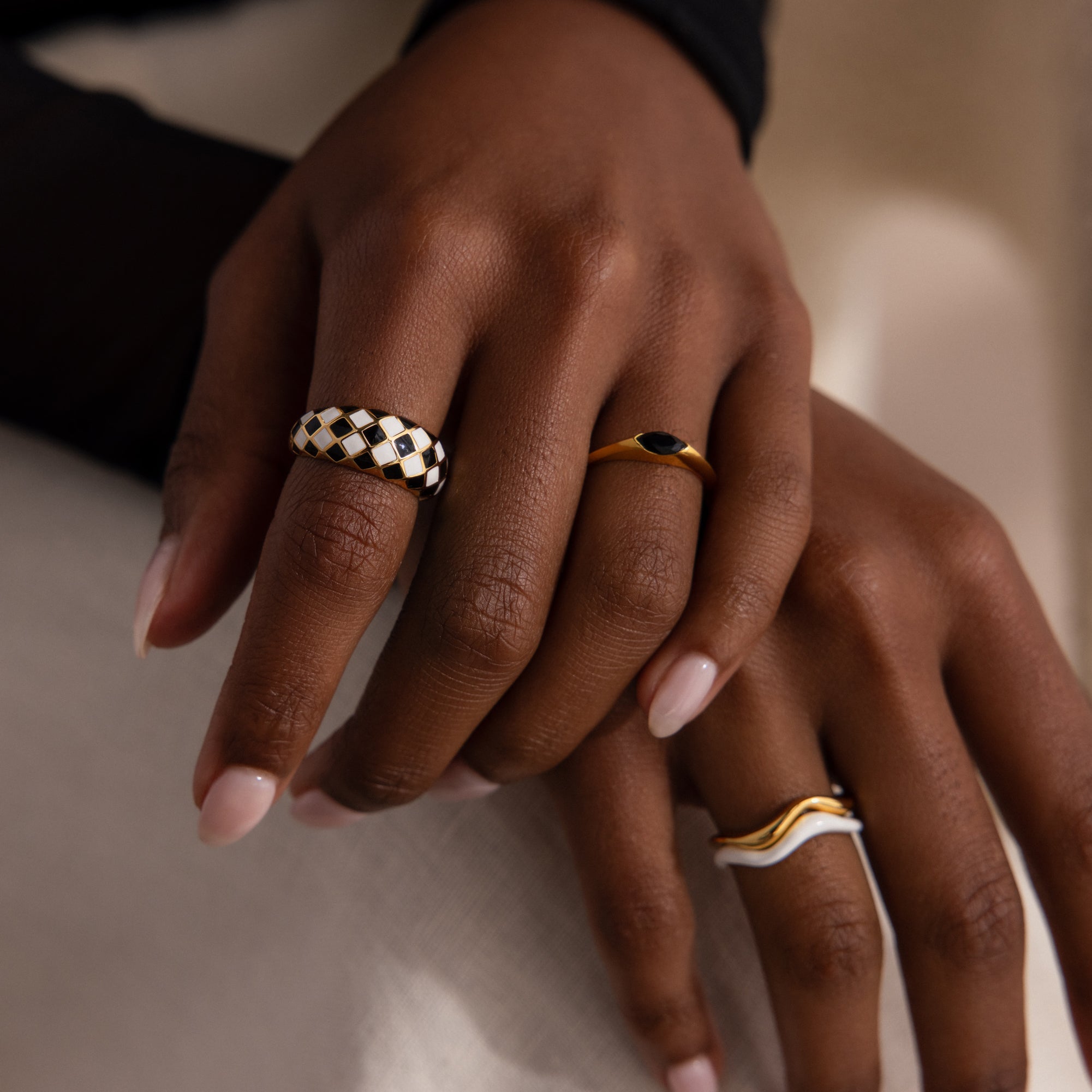 Model wearing a gold dome ring with black and white checkered enamel pattern, stacking with multiple gold rings.