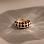 Gold dome ring with black and white checkered enamel pattern, displayed on a neutral surface.